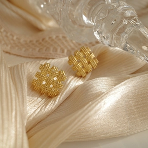 Macro shot of gold-tone woven square studs on elegant cream satin and lace background