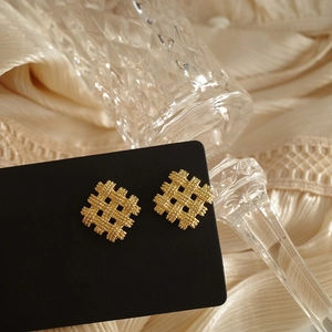 Macro view of woven square geometric stud earrings in gold finish on black card