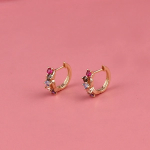 Golden huggie earrings with multi-colored zircon stones on a pink background