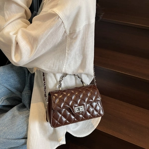 Sac bandoulière marron foncé matelassé avec chaîne et fermoir porté par un mannequin