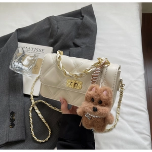 Detail view of cream quilted crossbody bag with gold chain strap and plush puppy charm