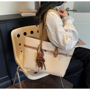 Detail of beige textured tote bag with dark brown straps and bear charm accessory
