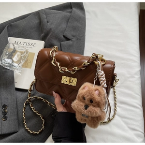 Detail of brown quilted crossbody bag with gold chain strap and plush puppy charm