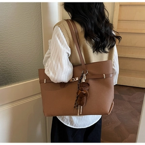 Brown leather tote bag with decorative belt strap and plush bear charm shown on model