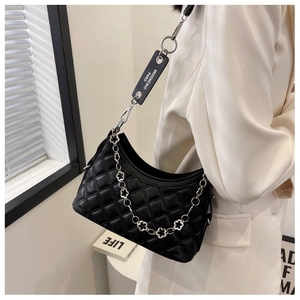 Detail of black quilted shoulder bag featuring decorative silver floral metal chain
