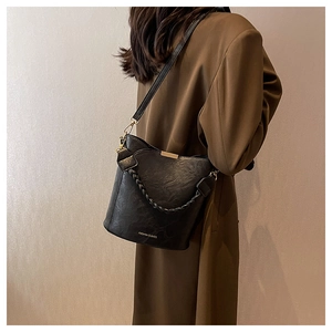 Détail du sac seau noir en cuir litchi avec poignée tressée et logo doré chic