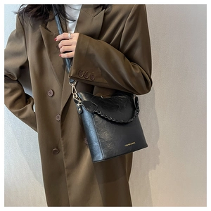 Détail d'un sac seau en cuir noir avec ferrures dorées et anse en chaîne porté par un mannequin