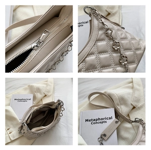Detail view of quilted leather texture and silver floral chain on a beige square bag