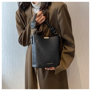 Détail du sac seau noir en cuir PU avec anse tressée et lettrage doré de mode