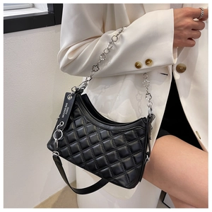 Detail of black quilted crossbody bag with silver chain strap worn by a model