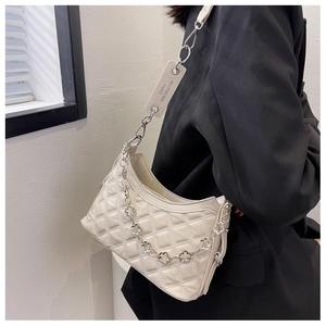 Detail of beige quilted crossbody bag with decorative silver floral chain and logo tag