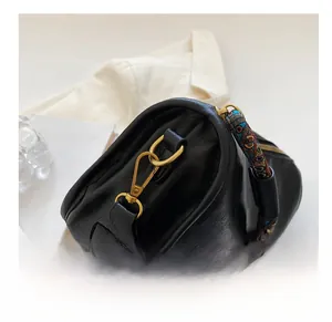 Détail du sac en cuir noir avec ferrures dorées et bandoulière tissée colorée
