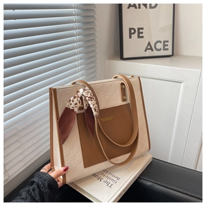 Detail of cream tote bag with grid texture, brown leather pocket, and leopard silk scarf