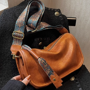 Détail d'un sac bandoulière en cuir marron avec une large sangle à motif géométrique
