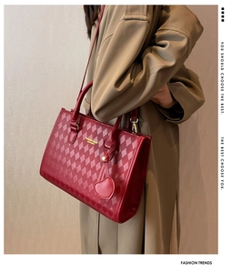 Detail of red quilted tote bag with gold lettering and heart charm on khaki trench coat