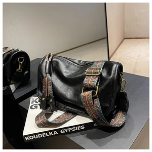 Détail d'un sac cylindre en cuir noir avec une large bandoulière jacquard de style bohème