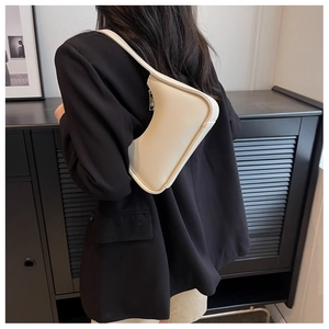 Model trägt eine cremefarbene halbmondförmige Schultertasche über einem dunklen Blazer