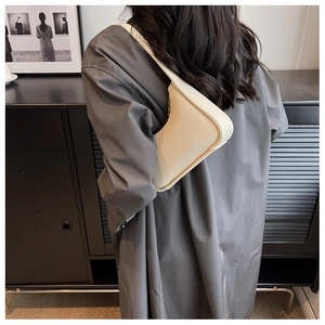 Minimalistische cremeweiße Baguette-Tasche über der Schulter an grauem Mantel