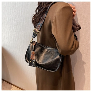 Détail du sac bandoulière en cuir noir avec sangle jacquard vintage sur un blazer marron