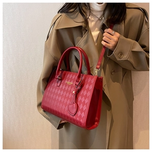 Detail of red quilted leather handbag with heart charm and golden hardware on trench coat
