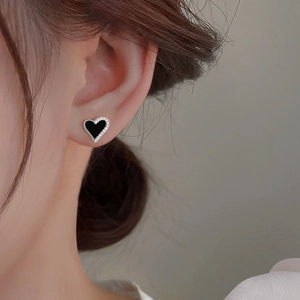 Close-up of asymmetrical black enamel and rhinestone heart earrings worn by a model