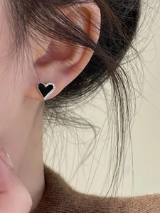 Close-up of heart-shaped black enamel earrings with shimmering rhinestones worn on ear
