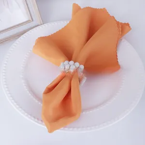 Close-up of hand-woven pearl napkin ring with orange textile on a beaded plate