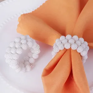 Elegant hand-woven white pearl napkin ring on orange fabric for festive wedding decor