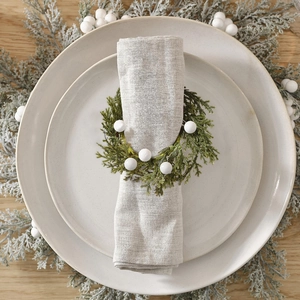 Detail of Christmas napkin ring featuring faux pine leaves and white berries on linen