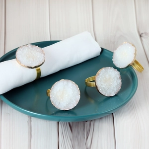 Set of 4 white crystal cluster napkin rings with gold metal accents on a dinner plate