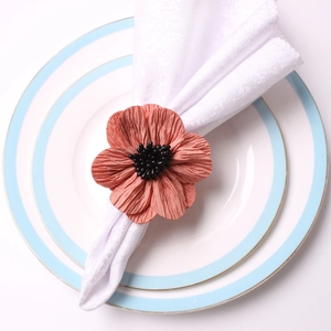 Detail of coral pink fabric flower napkin ring with black bead center on ceramic plate