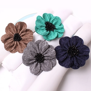 Detail of four fabric flower napkin rings with fringe edges and beaded centers on linen