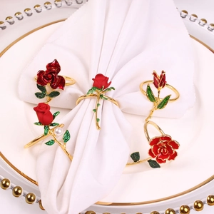 Elegant red rose napkin rings with gold metal bands and green crystals on white dinnerware