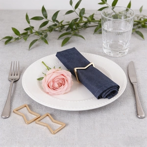 Elegant gold M-shaped metal napkin rings set on white plates with blue linens