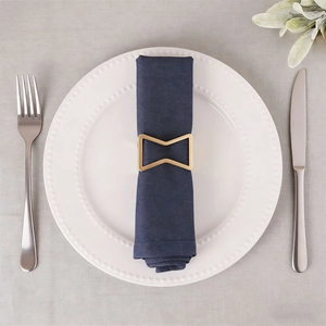 Golden bow napkin ring on navy fabric with white porcelain plate and cutlery