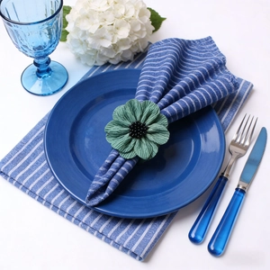 Green fabric flower napkin ring with ruffled petals on a blue plate table setting