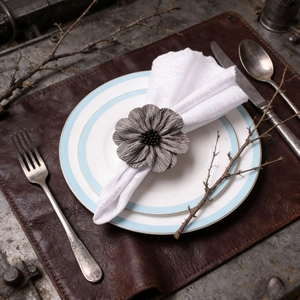 Handmade grey fabric flower napkin ring with black bead center on an elegant table setting