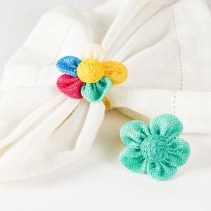 Dettaglio di portatovaglioli a fiori intrecciati colorati con anelli in metallo dorato