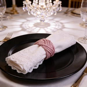 Pink woven knot napkin ring with silky luster on a white lace napkin and black plate
