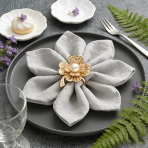 Luxury gold four-leaf flower napkin ring with pearl on a grey linen table setting