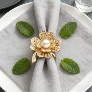 Close-up of golden clover napkin ring with pearl on grey fabric napkin and white plate