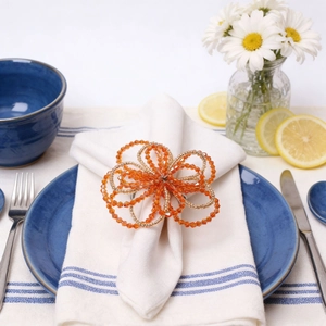 Handmade orange floral beaded napkin ring on white linen with elegant tableware