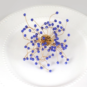 Handmade gold wire napkin ring with dark blue crystal beads on white ceramic plate