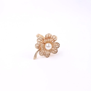 Golden flower napkin ring with central pearl and hollowed petals on white background