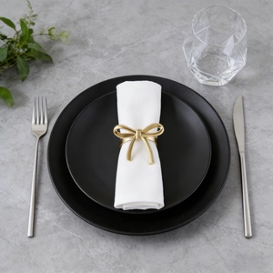 Golden bow napkin ring on white fabric napkin set on a modern black plate dinner table