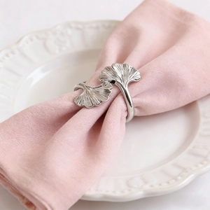 Silver gingko leaf napkin ring with polished metal finish on elegant pink fabric