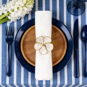 Close-up of golden floral napkin ring with cream petals on blue striped linen