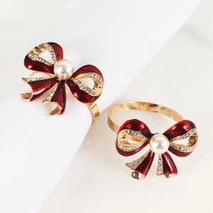 Detailed view of red enamel bow napkin rings with pearls and rhinestones on white cloth