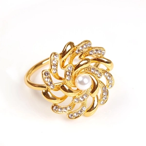 Gold floral napkin ring with white pearl center and sparkling rhinestones on white background