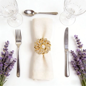Elegant gold flower napkin ring with central pearl and rhinestones on a white napkin